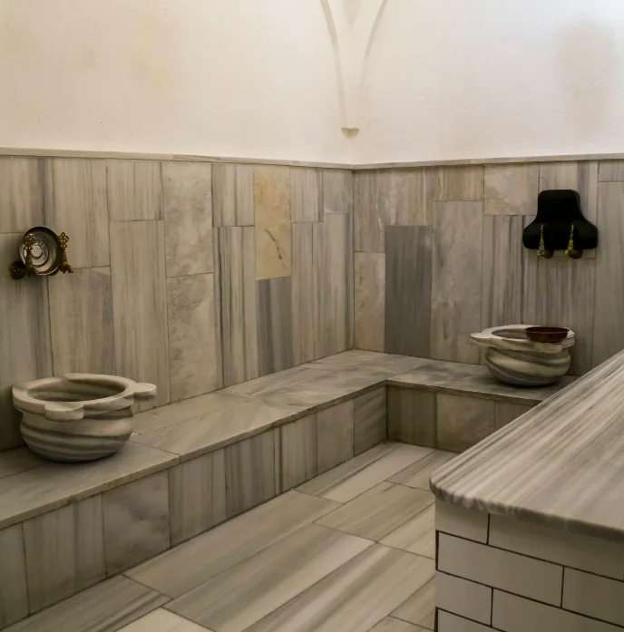 Marble bathing room with two traditional kurnas and wall-mounted brass taps.