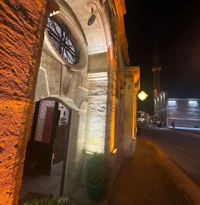 Side entrance and oval ironwork window of Ürgüp Hamam illuminated at night.