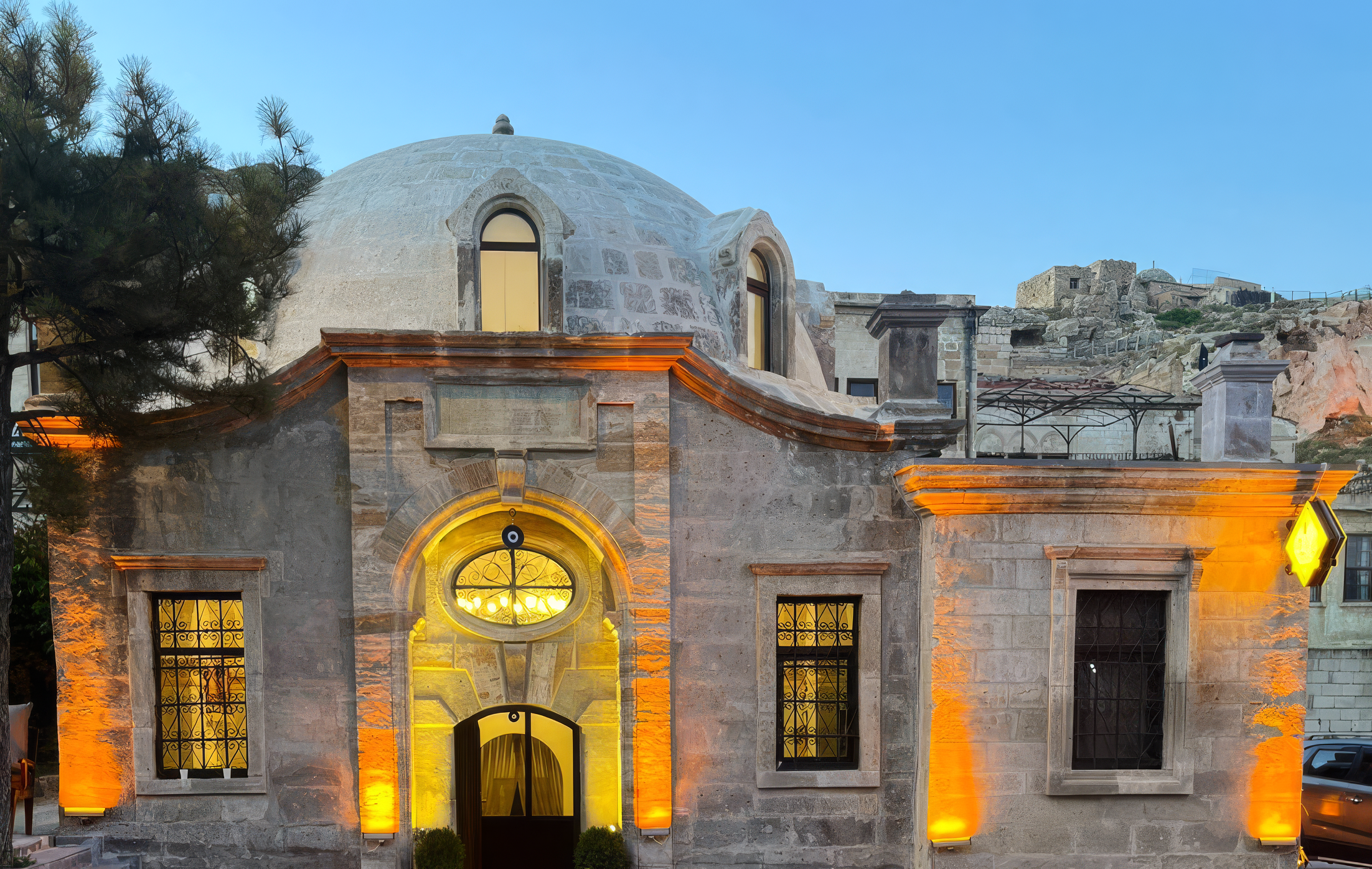 Cut-stone exterior of Ürgüp Hamam at blue hour, illuminated with warm amber light.